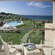 A balcony with a seating area overlooking a pool area near a forest and the ocean
